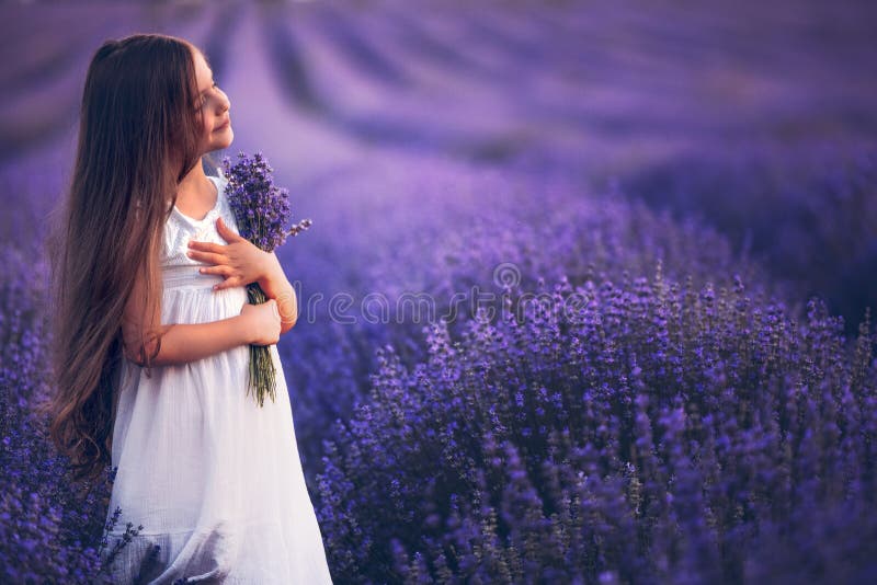 Happy little girl with dress enjoying lavender field with bouquet of flowers