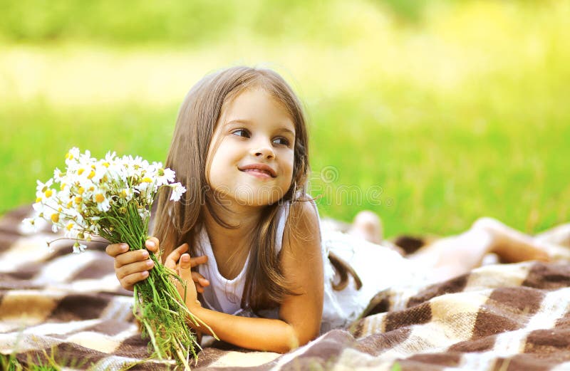 Happy little girl and flowers on the meadow in summer sunny day