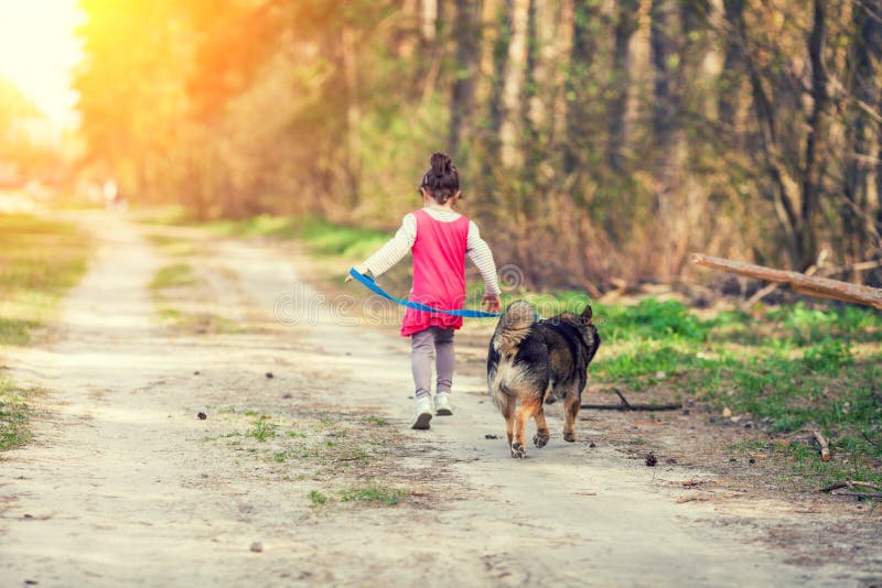 Little girl playing with a dog running on dirt road along forest