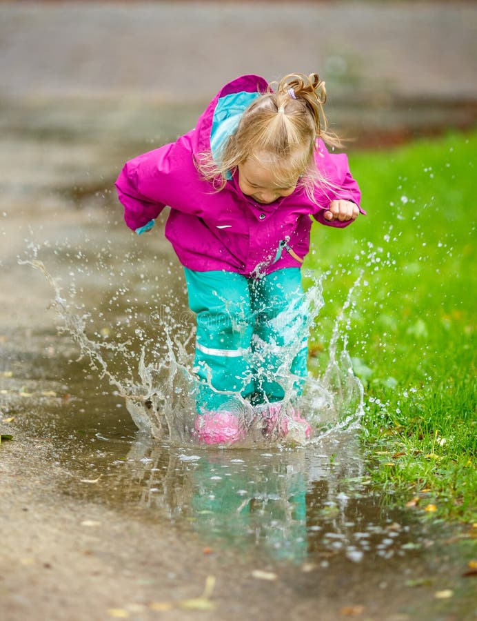 Happy little girl jumps into a puddle.
