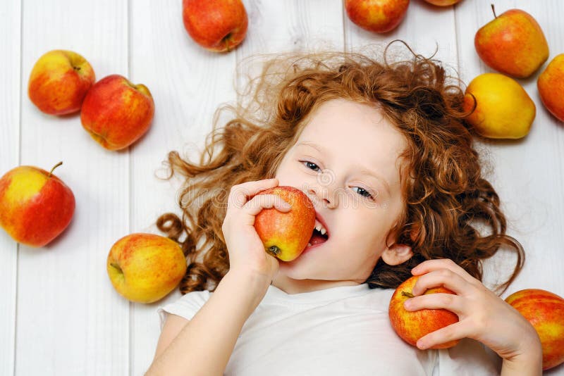 Happy little girl with red apples on light wooden floor. Top vie