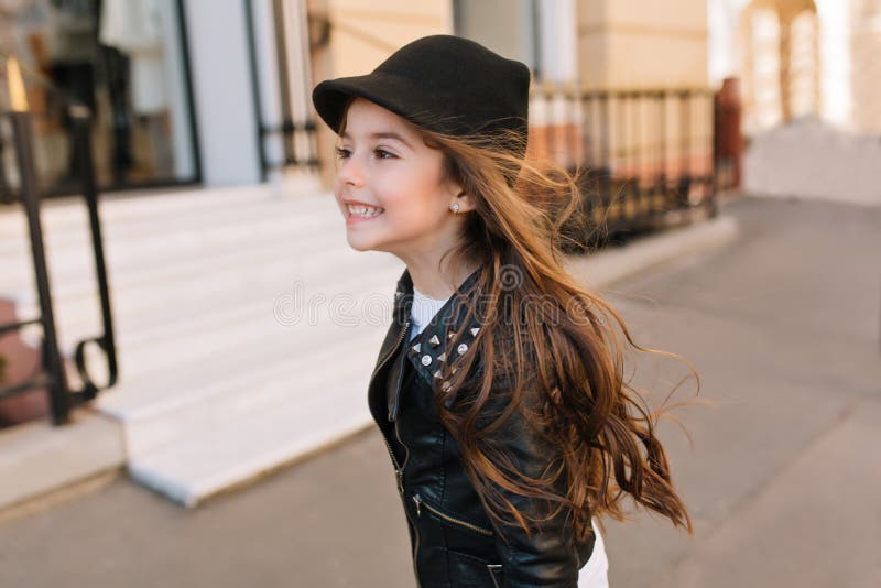 Happy little girl running down the street with dark hair waving and looking away. Portrait of playful brunette girlie stock photo Happy little girl running down the street with dark hair waving and looking away. Portrait of playful brunette girlie stock photo