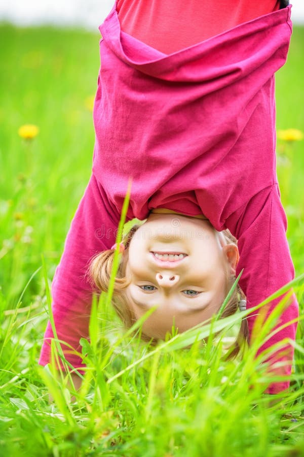 Happy little girl standing upside down on grass in summer park royalty free stock photos Happy little girl standing upside down on grass in summer park royalty free stock photos