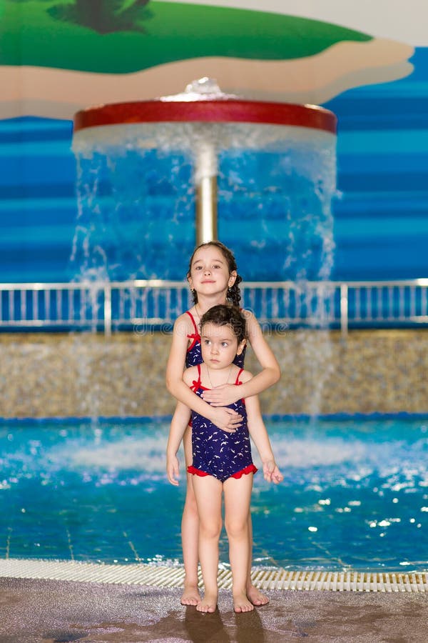 Happy little girls in identical swimsuits posing near the children`s pool in the water Park. Child learns to swim.