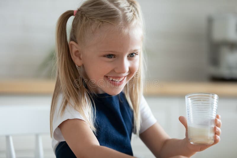 Happy little preschool girl holding glass of fresh milk.