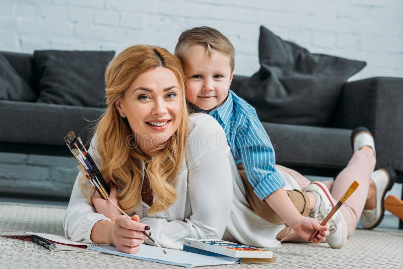 Happy little son sitting on mother back while she painting