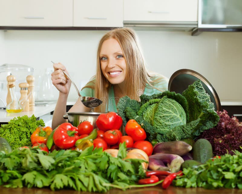 Happy long-haired woman cooking with heap of vegetables