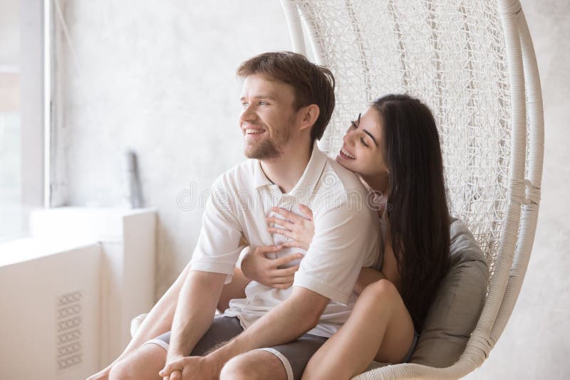 Happy loving couple sitting together in lounge hanging chair. Attractive girlfriend embracing dreaming smiling boyfriend, sitting behind his back, women royalty free stock image Happy loving couple sitting together in lounge hanging chair. Attractive girlfriend embracing dreaming smiling boyfriend, sitting behind his back, women royalty free stock image
