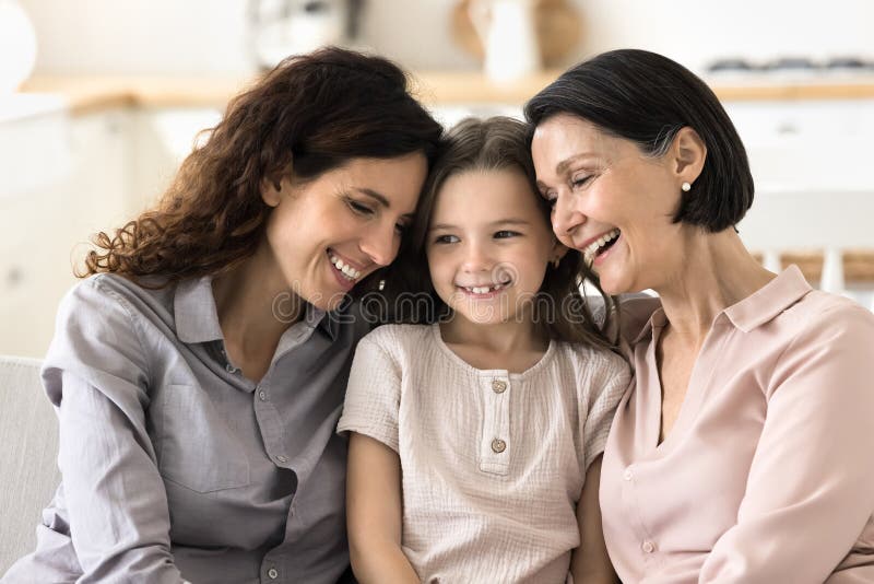 Happy lächelnd kleines Mädchen sitzt auf Couch zwischen Mutter Großmutter lizenzfreies stockbild