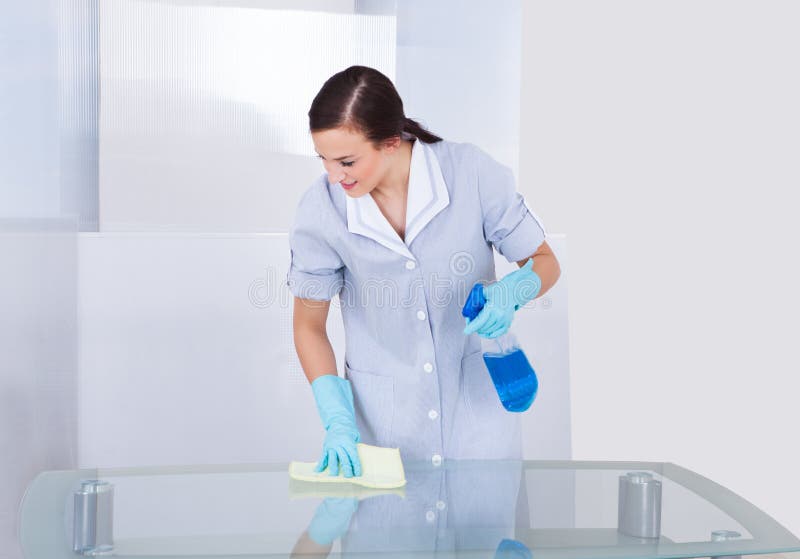 Happy maid cleaning glass table royalty free stock photo