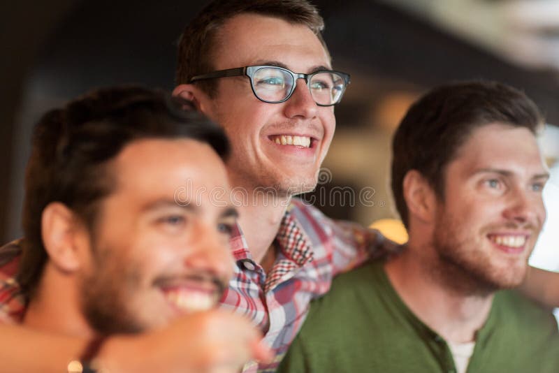 Happy male friends watching football at bar or pub