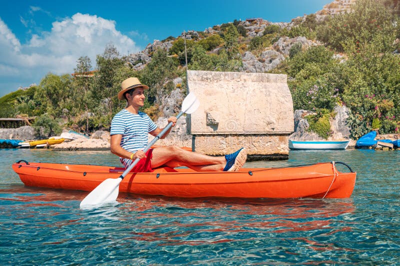Happy male traveler kayaks near an ancient sarcophagus and a Lycian tomb in the sunken city of Kekova in Turkey. A pleasant and stock images
