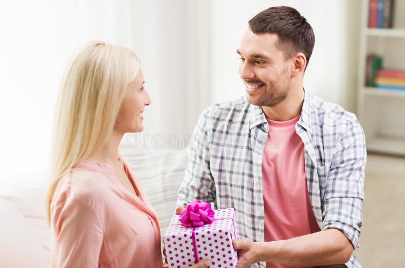 Happy man giving woman gift box at home. Couple, latin.