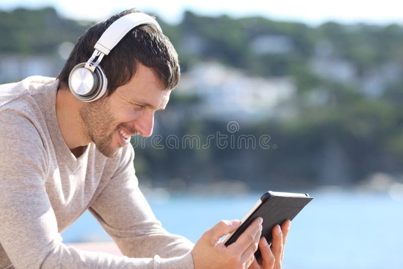 Happy man listening music with headphones on tablet on the beach