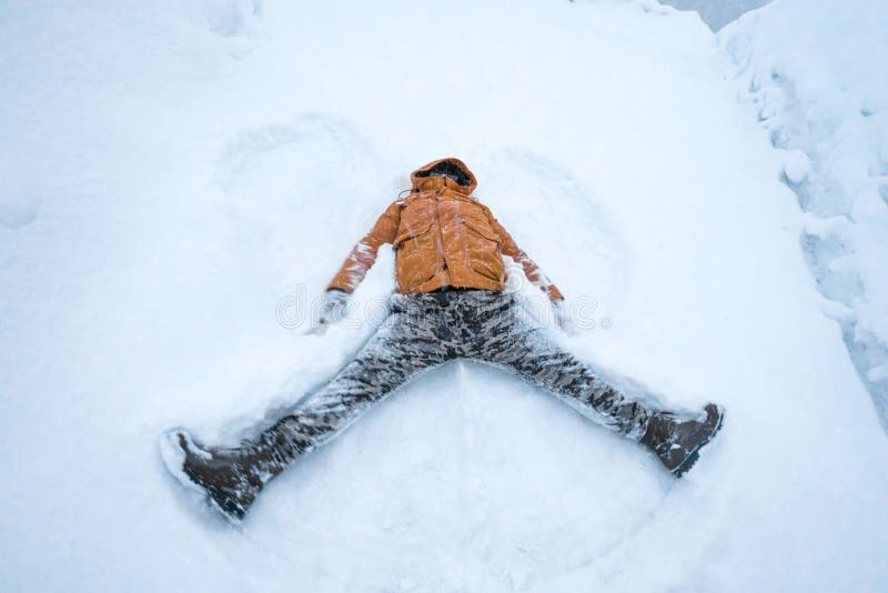 Happy man lying down on the snow in winter. People, smiling.