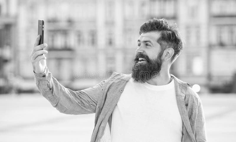 Happy man making video call through mobile Internet outdoors. Bearded man smiling to smartphone stock photos