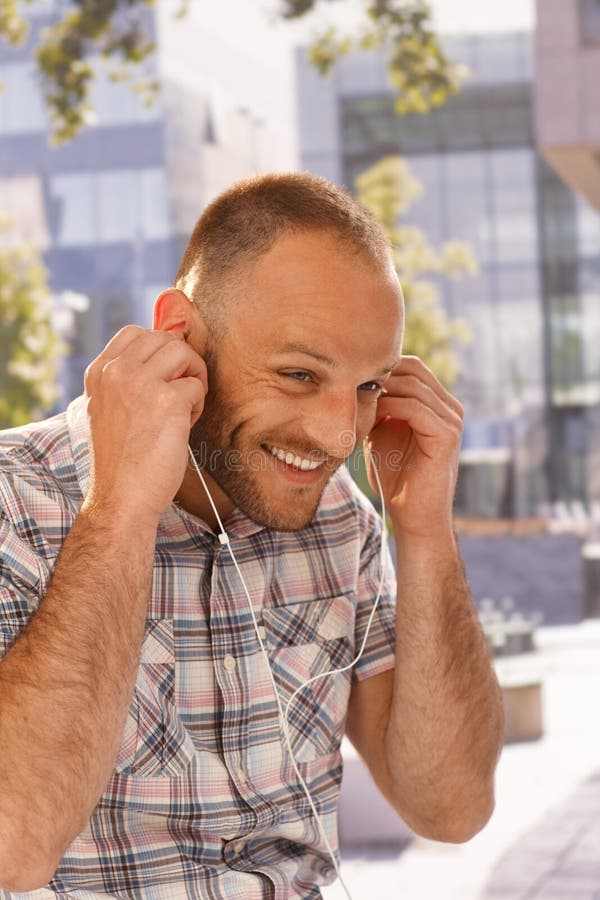 Happy man putting in earbuds, smiling outdoors.