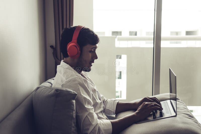 Happy man relaxing on the sofa listening to music with laptop at home