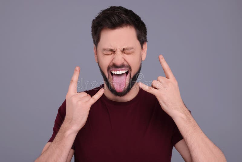 Happy man showing his tongue and making rock gesture on light grey background royalty free stock image