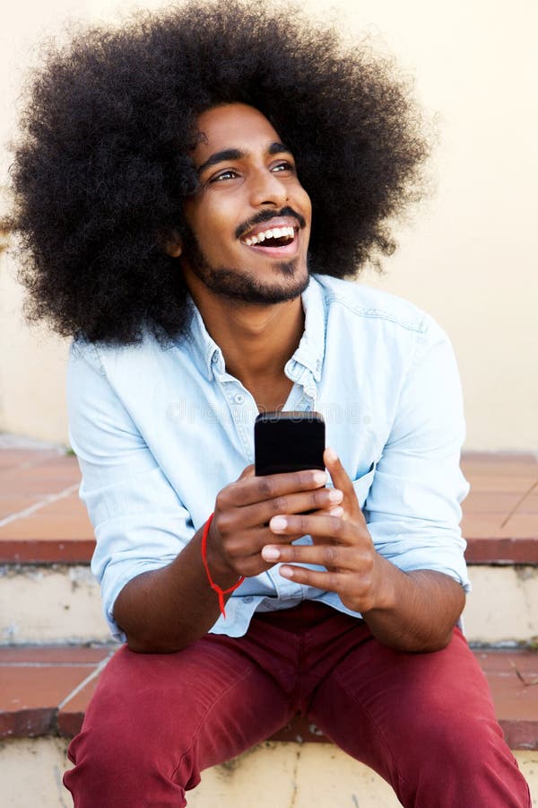 Happy man sitting on steps with mobile phone laughing