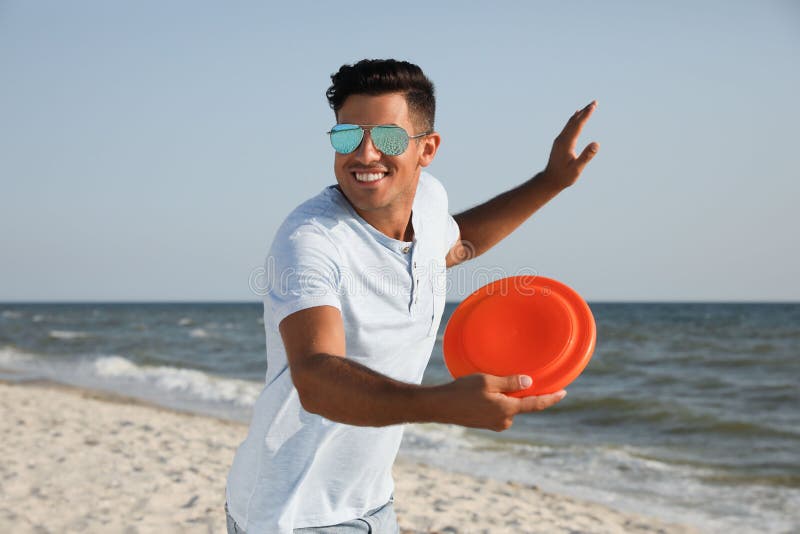 Happy Man Throwing Flying Disk at Beach on Sunny Day Stock Photo