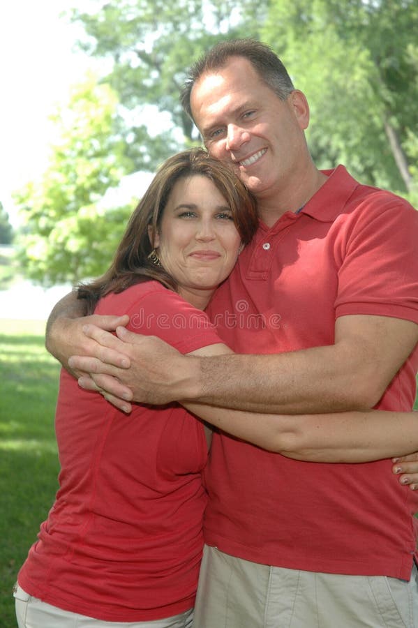 Portrét šťastne ženatý pár stredného veku, obe nedbalo oblečená v červenej košele a béžové nohavice, objímať sa navzájom.