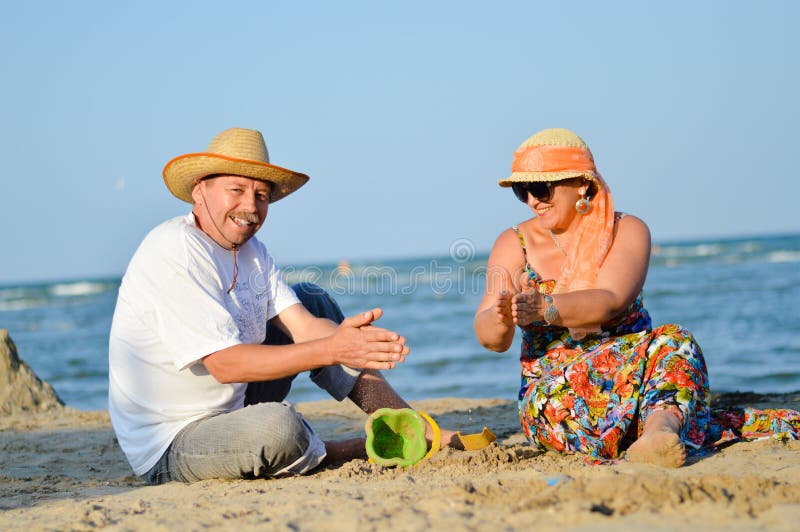 Happy Mature Couple Having Fun Sitting At Seashore On Sandy Beach Stock