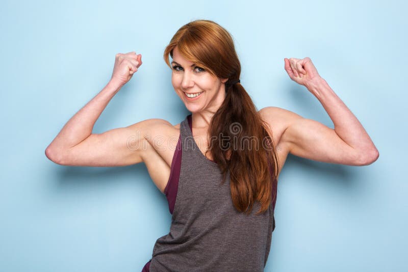 Portrait of happy mature woman flexing bicep muscles against blue wall