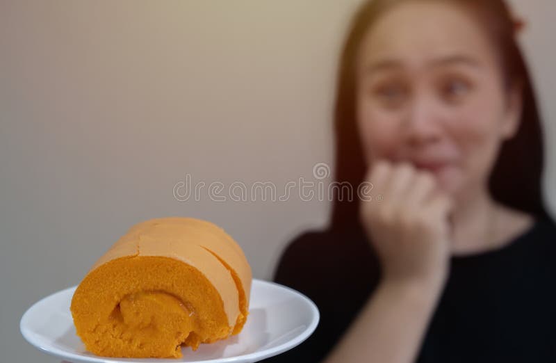 Happy middle aged Asian woman eating orange cake and excited, winner expression celebrating victory screaming with big smile and raised hand. Selective focus, copy space