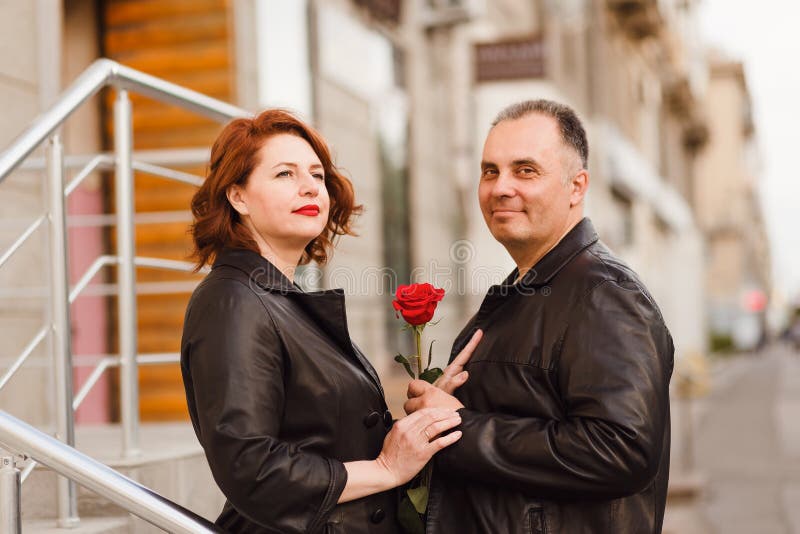 Happy middle-aged man and woman holding red rose. Love in town