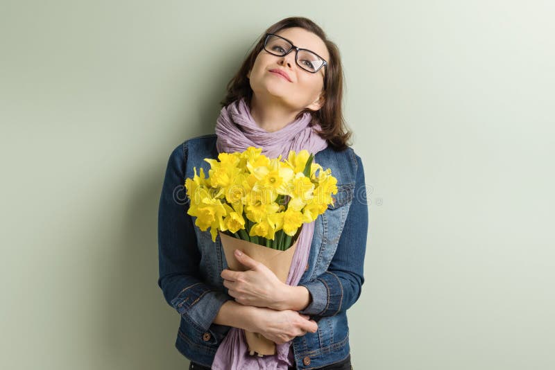 Happy middle aged woman with bouquet of yellow flowers, green wall background