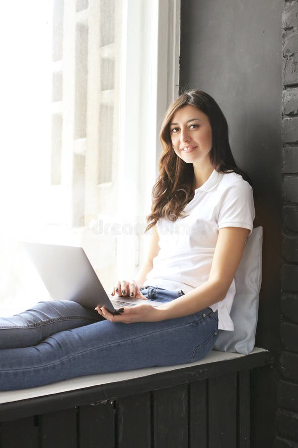 Happy millennial girl w/ laptop on windowsill. Portrait of young woman with diastema gap between teeth. Beautiful smile. Minimal i royalty free stock photo Happy millennial girl w/ laptop on windowsill. Portrait of young woman with diastema gap between teeth. Beautiful smile. Minimal i royalty free stock photo