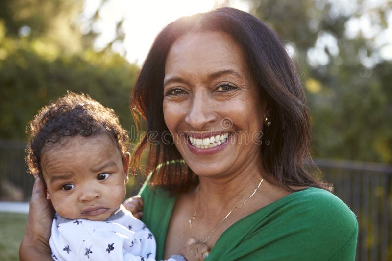 Happy African American middle aged grandmother holding her three month old grandson in the garden and smiling to camera, close up royalty free stock photography Happy African American middle aged grandmother holding her three month old grandson in the garden and smiling to camera, close up royalty free stock photography