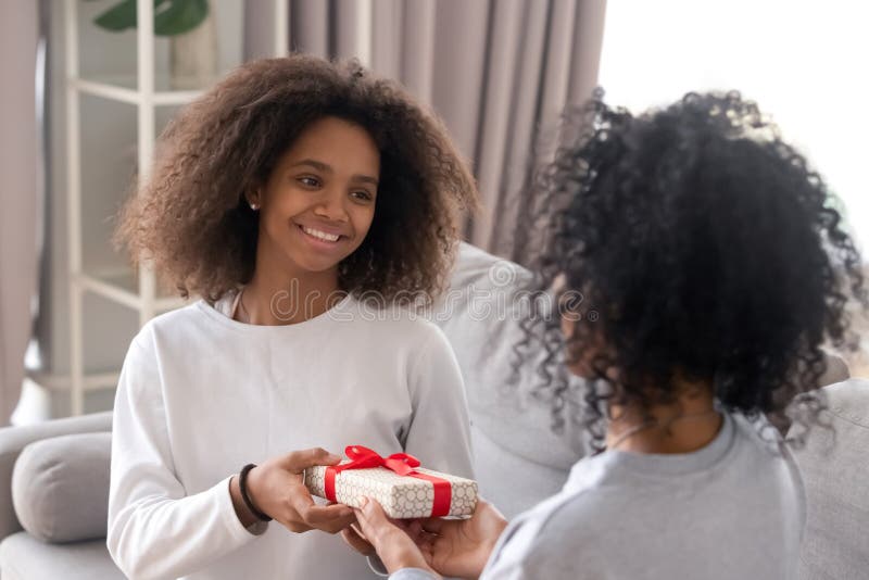 Happy african teen daughter give birthday gift box to mum