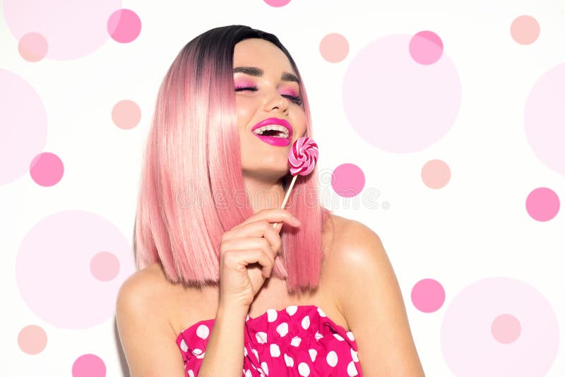 Happy model girl eating lollipop. Beauty Glamour young woman with trendy pink hair style and beautiful makeup