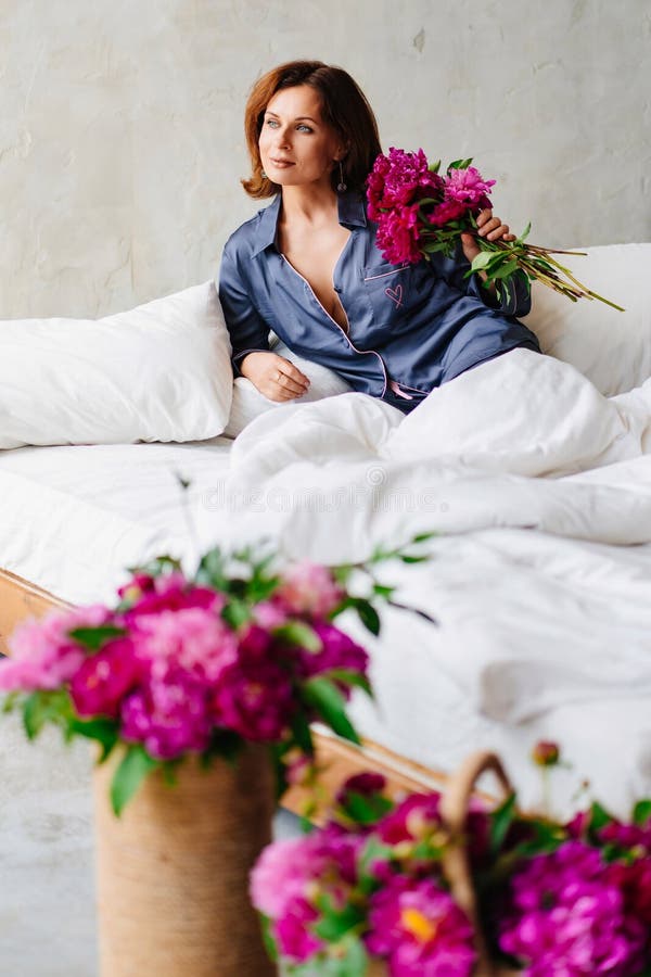 happy morning. a woman in pajamas in bed with a peonies.