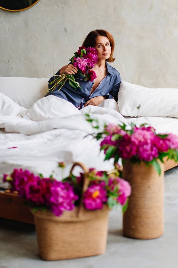 happy morning. a woman in pajamas in bed with a peonies.