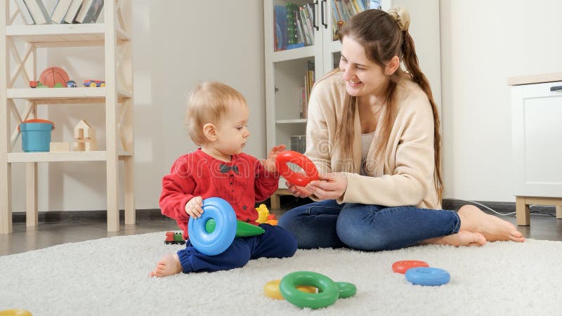 Happy mother with child building toy tower on soft carpet at home. Baby development, child playing games, education and learning