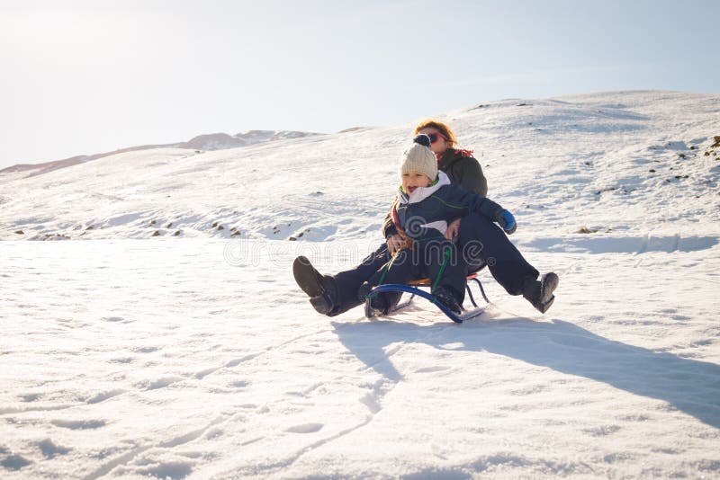 Happy mother and child playing in the snow with a sledge