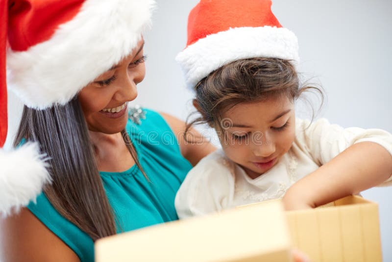 Christmas, holidays, family, childhood and people concept - happy mother and little girl in santa hats opening gift box at home. Christmas, holidays, family, childhood and people concept - happy mother and little girl in santa hats opening gift box at home