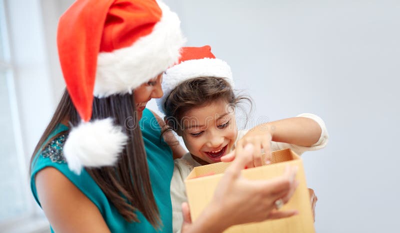 Christmas, holidays, family, childhood and people concept - happy mother and little girl in santa hats opening gift box at home. Christmas, holidays, family, childhood and people concept - happy mother and little girl in santa hats opening gift box at home