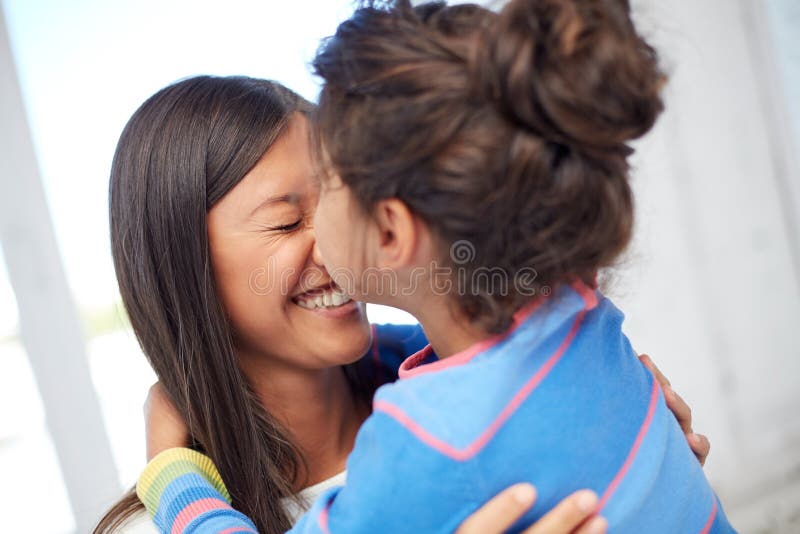 Family, children, love and happy people concept - happy little girl hugging mother and kissing her on nose at home. Family, children, love and happy people concept - happy little girl hugging mother and kissing her on nose at home