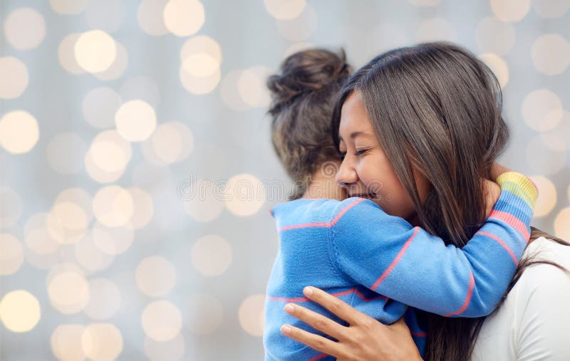 Family, children, love and happy people concept - happy mother and daughter hugging over lights background