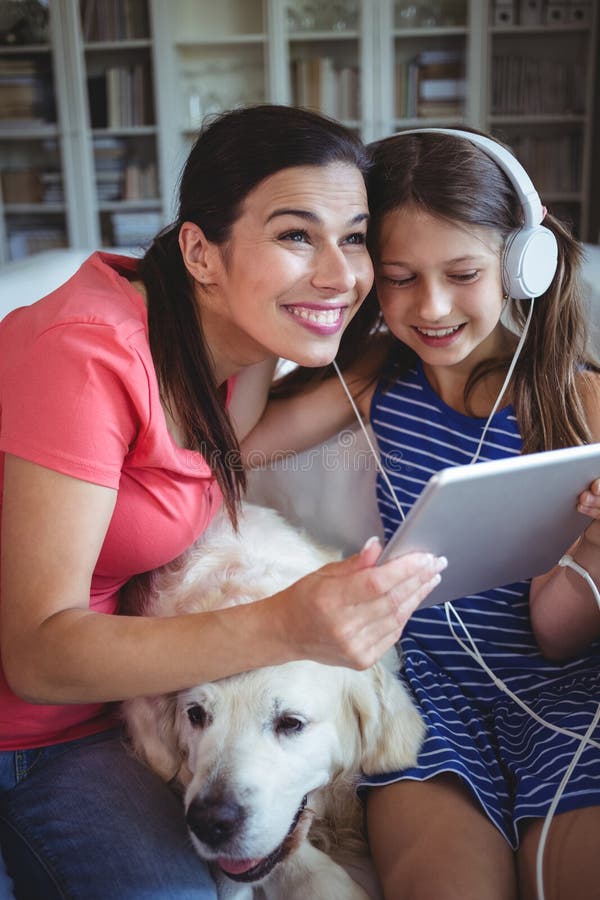 Happy mother and daughter sitting with pet dog and listening to music on headphones