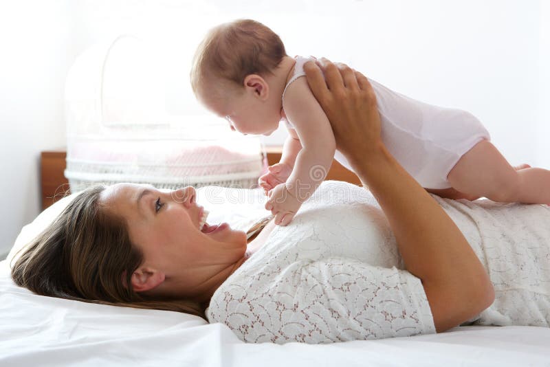 Happy mother playing with cute baby in bed