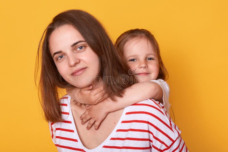 Happy mother`s day! Child daughter hugging mom from behind. Mum wearing striped shirt and little girl looking at camera with happ royalty free stock images Happy mother`s day! Child daughter hugging mom from behind. Mum wearing striped shirt and little girl looking at camera with happ royalty free stock images