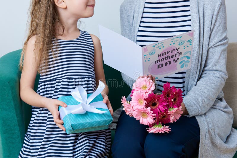 Happy Mother`s Day. Cute little girl giving mom greeting card, present and bouquet of pink gerbera daisies. Mother and daughter.