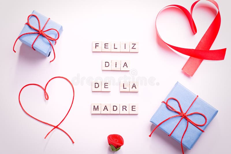 Happy Mother`s Day greeting card with red hearts, blue gift boxes and golden confetti on pastel table top, overhead shot. Feliz. Dia de la madre text from royalty free stock image