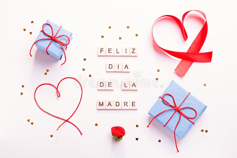 Happy Mother`s Day greeting card with red hearts, blue gift boxes and golden confetti on pastel table top, overhead shot. Feliz. Dia de la madre text from stock photography