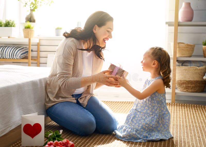 Happy mother`s day! Child daughter is congratulating mom and giving her flowers tulips. Mum and girl smiling. Family holiday and togetherness